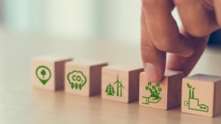 Holzklötzchen mit bedruckten Symbolen: Fabrik, Geld, Windenergieranlagen, CO2, Baum